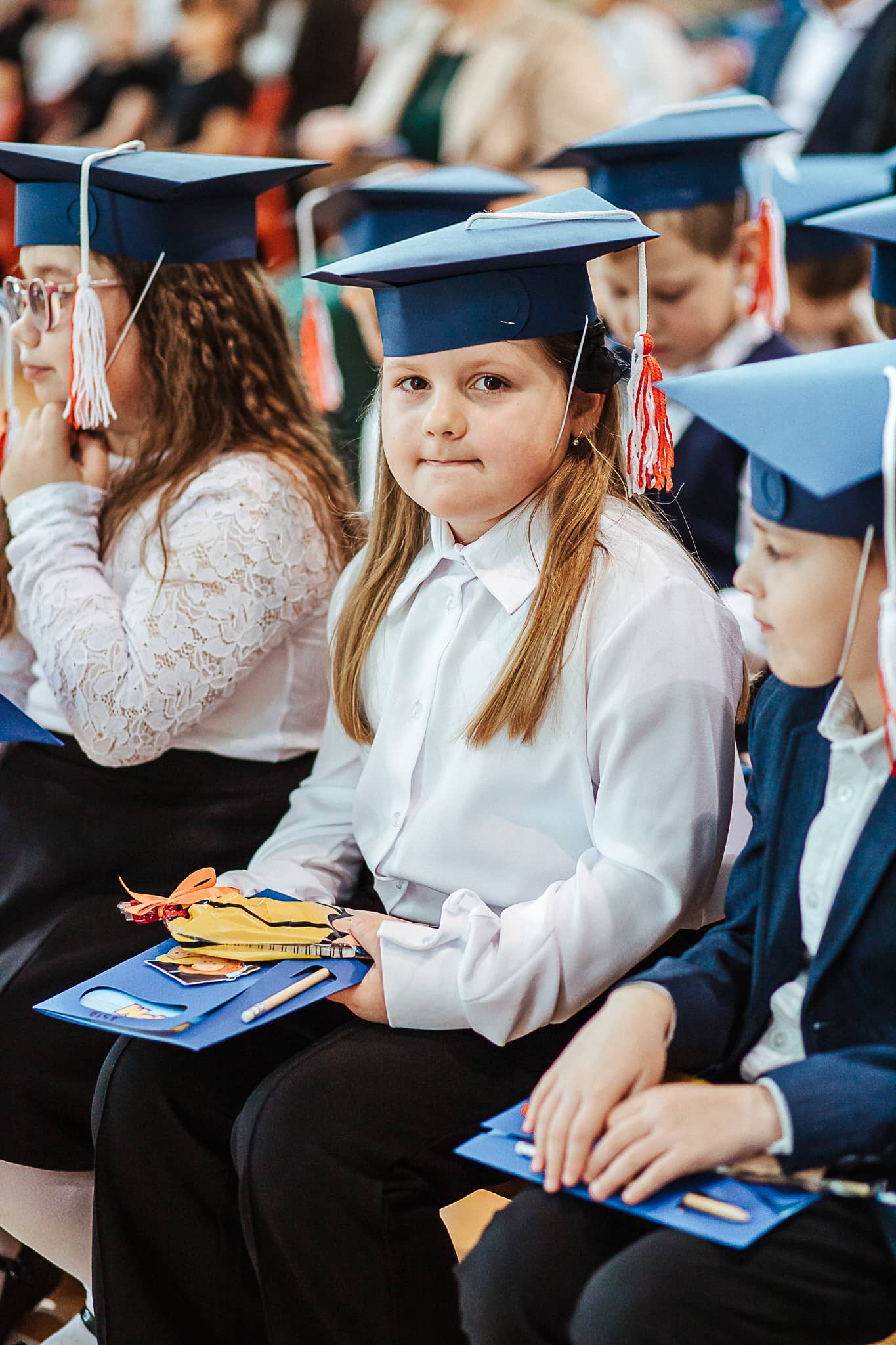 Zbliżenie na uczniów siedzących na sali gimnastycznej po zakończeniu uroczystości ślubowania