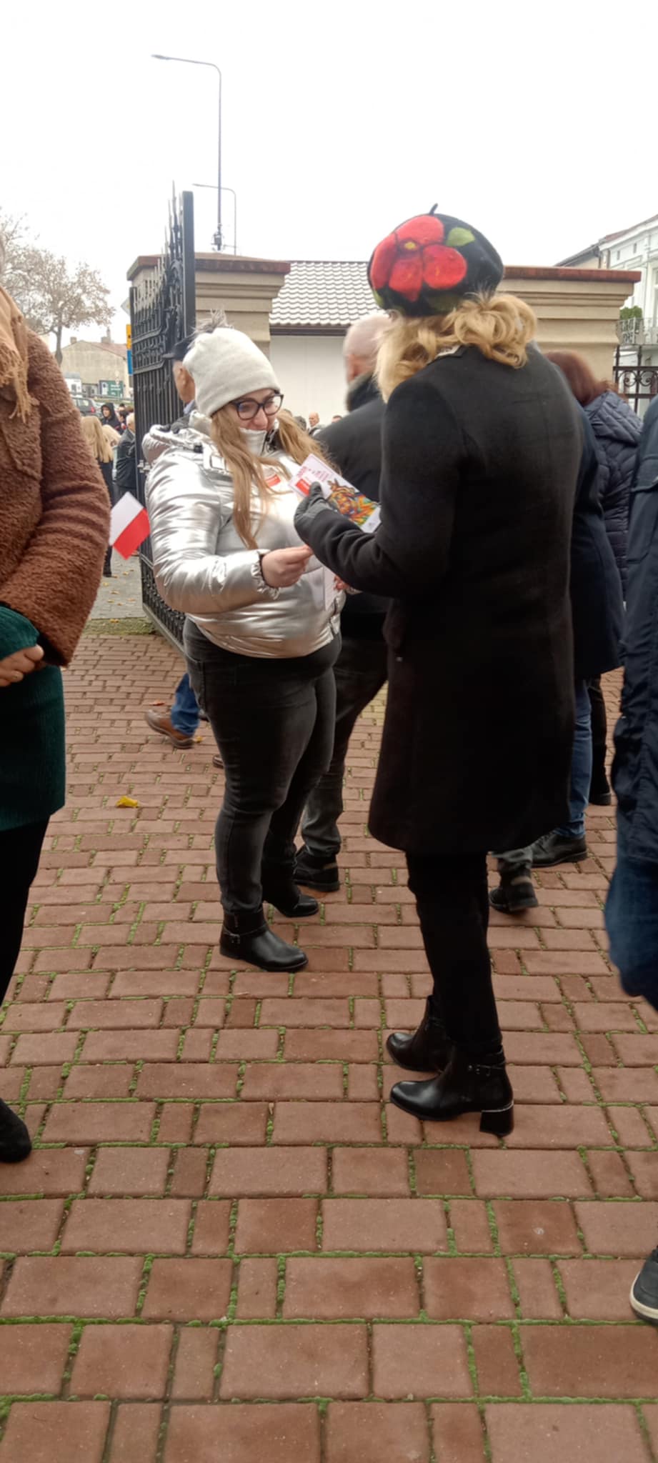 Uczennica wręcza materiały patriotyczne podczas gminnych obchodów Narodowego Święta Niepodległości