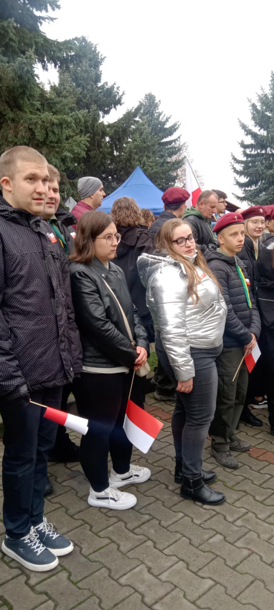 Uczniowie stoją w apelu, trzymając polskie flagi, w czasie uroczystości z okazji Narodowego Święta Niepodległości