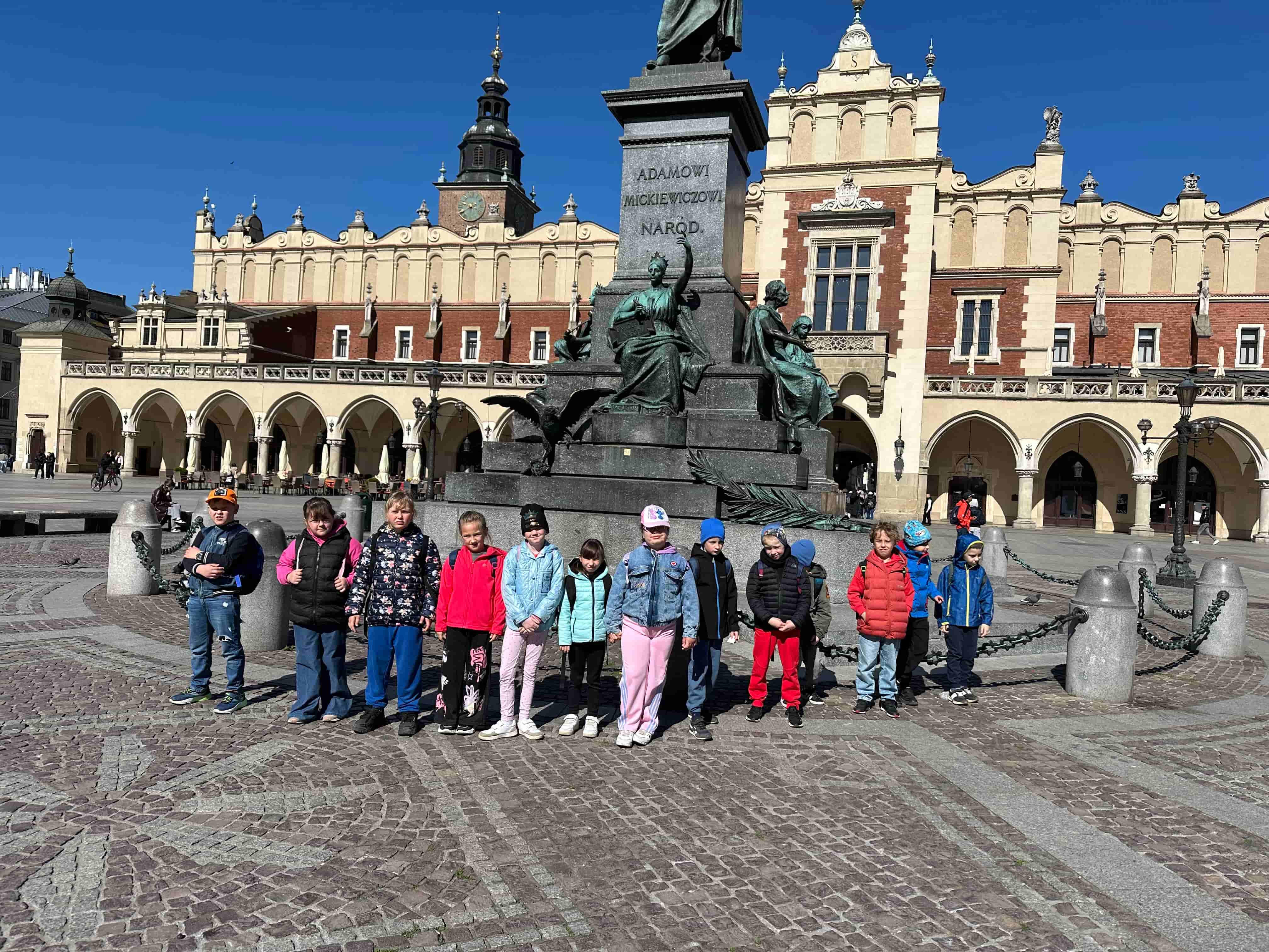 Uczniowie stoją przed krakowskimi Sukiennicami podczas wycieczki edukacyjnej