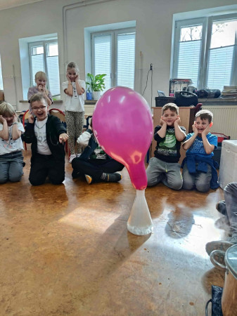 Grupa dzieci zatyka uszy w oczekiwaniu na huk pękającego balonu podczas eksperymentu chemicznego, zdjęcie 2 z 5