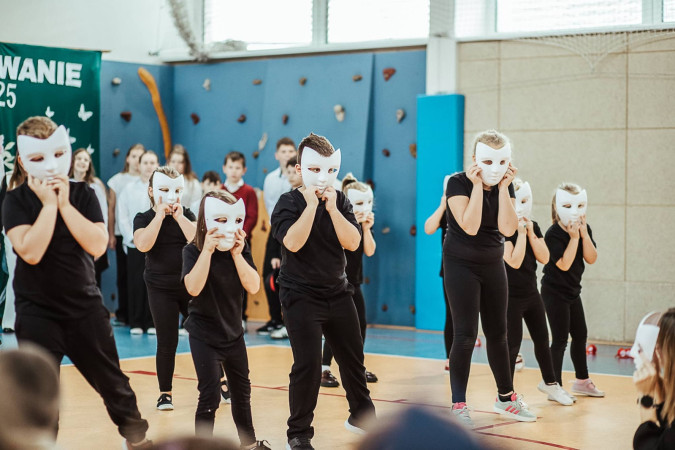 Uczniowie ubrani na czarno z białymi maskami występują podczas szkolnych obchodów Dnia Edukacji Narodowej, zdjęcie 4 z 5