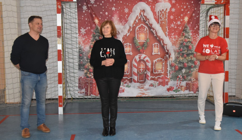 Przedstawiciel seniorów oraz dwoje nauczycieli na tle świątecznego plakatu w sali gimnastycznej, zdjęcie 1 z 5