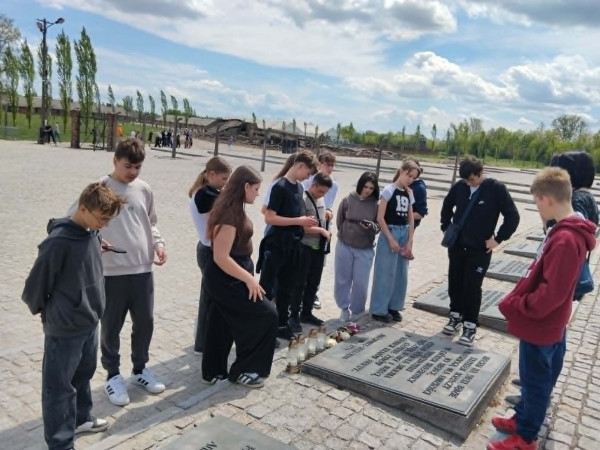 Uczniowie stoją przed tablicą upamiętniającą ofiary obozu Auschwitz-Birkenau, zdjęcie 1 z 5