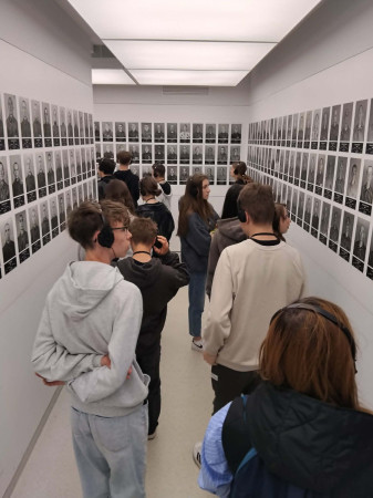 Uczniowie przechodzą korytarzem z fotografiami więźniów obozu koncentracyjnego, zdjęcie 3 z 5