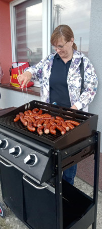 Opiekun przygotowuje kiełbaski na grillu dla uczestników spotkania, zdjęcie 5 z 5